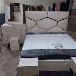 طرح پارچه‌ای یا چرمی روشن (کرم/بژ)، با طرح هندسی (لوزی/شش ضلعی) و نوار طلایی، پاتختی‌ها و کنسول ست با پایه‌های طلایی فانتزی